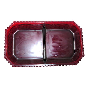 May include: A rectangular ruby red glass serving dish featuring a central divider and a scalloped edge. The exterior rim displays a pressed geometric pattern, while the interior surface is smooth and translucent, showcasing the deep red color.