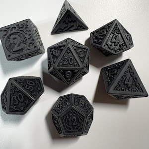 May include: A set of seven black polyhedral dice for tabletop gaming. Each die features engraved numbers and decorative patterns. The dice include a d4, d6, d8, d10, d12, d20, and a percentile die.