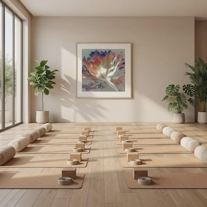 Op de afbeelding: Een yogastudio met beige yogamatten, blokken en riemen in rijen gerangschikt. Een grote ingelijste bloemenprint hangt aan de muur. Planten in neutrale potten en bolsterkussens dragen bij aan de serene sfeer. De kamer heeft een lichte houten vloer.