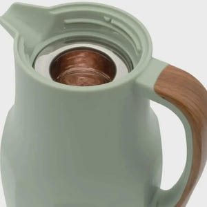 May include: A pale green insulated jug with a wooden handle. The jug has a stainless steel interior and a pouring spout. The handle is made of wood-grain material. The jug is designed to keep drinks hot or cold.