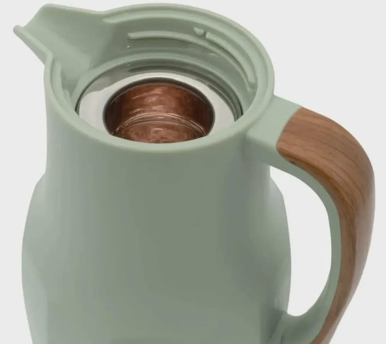 May include: A pale green insulated jug with a wooden handle. The jug has a stainless steel interior and a pouring spout. The handle is made of wood-grain material. The jug is designed to keep drinks hot or cold.