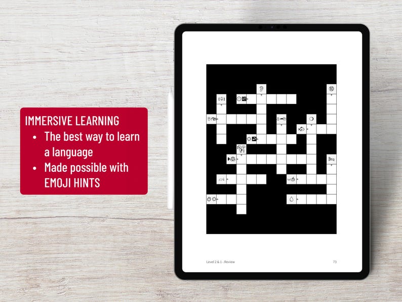 K&ouml;nnte beinhalten: Ein digitales Tablet mit einem schwarz-wei&szlig;en Kreuzwortr&auml;tsel mit Emoji-Hinweisen. Der Bildschirm zeigt den Text "Level 2.6.1 Review" und "73". Ein rotes Rechteck links zeigt "IMMERSIVE LEARNING" und "The best way to learn a language. Made possible with EMOJI HINTS."