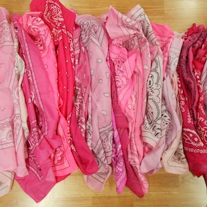 May include: A collection of pink bandanas in various shades, from light to deep rose. Each bandana features a paisley pattern in white or black, creating a visually appealing display of textiles.