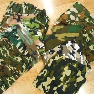 May include: A pile of camouflage fabric squares in various shades of green, brown, and beige. The fabric is folded and stacked, creating a textured and layered effect.