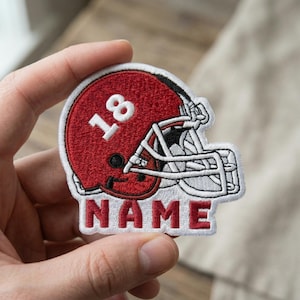 May include: Embroidered patch featuring a red football helmet with the number 18 in white. The word "NAME" is embroidered in red below the helmet. The patch has a white border.