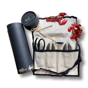 May include: A seafood tool set with a canvas roll, black and gold packaging, and decorative lobster and crab figurines. The canvas roll contains various tools, including a hammer and shell crackers. The packaging features the text "Down the Cove".