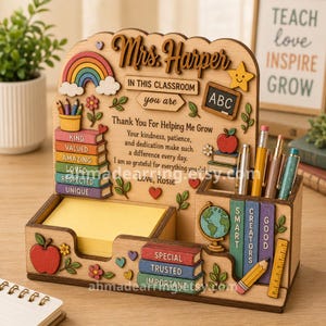 May include: A wooden desk organiser featuring a rainbow, a chalkboard with ABC, and stacked book cutouts labelled with words like Kind, Valued, and Special. It includes a yellow notepad holder, a pen cup, and text reading Mrs. Harper In This Classroom you are Thank You For Helping Me Grow.