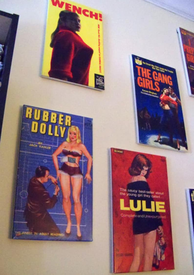 May include: A wall display of vintage paperback books with titles like "WENCH!" "Rubber Dolly" "The Gang Girls" and "LULIE". The covers feature illustrations of women in various poses.
