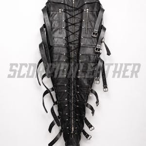 May include: A black leather full-body restraint suit featuring a central vertical zipper, extensive black lace-up detailing, multiple adjustable buckled straps along the sides, and two zippered chest pockets. The text SCORPION LEATHER is visible.