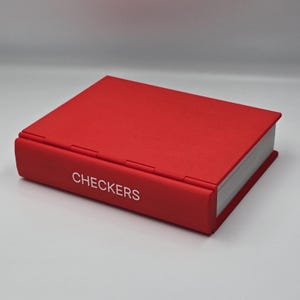 Puede incluir: Un juego de damas rojo. La caja del juego es rectangular con la palabra "CHECKERS" impresa en blanco en el lateral. La caja está cerrada y parece estar hecha de un material texturizado.