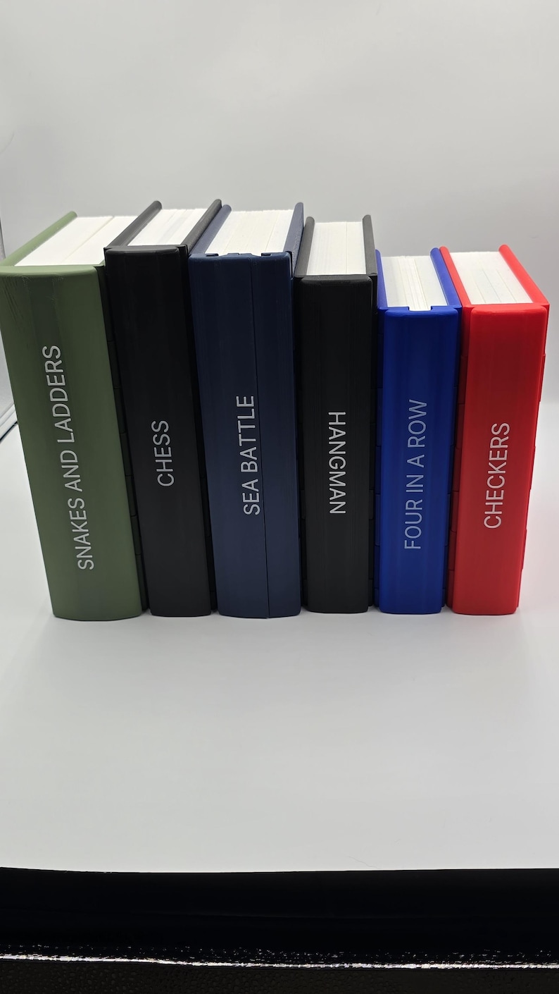 May include: A collection of six board game books with white pages and colorful spines. The titles include "Snakes and Ladders", "Chess", "Sea Battle", "Hangman", "Four in a Row", and "Checkers". The spines are in various colors, including green, black, blue, and red.