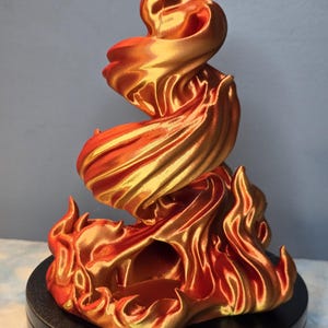 Puede incluir: Escultura impresa en 3D de una llama, con un diseño dinámico y arremolinado. La escultura es principalmente naranja y dorada, con un acabado brillante. La base es negra, proporcionando contraste con los colores de fuego. Un artículo decorativo.