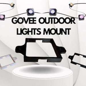 Puede incluir: La imagen muestra el texto "GOVEE OUTDOOR LIGHTS MOUNT" sobre tres soportes de montaje. Los soportes son negros y blancos. Encima del texto hay pequeñas luces cuadradas en un cable negro.