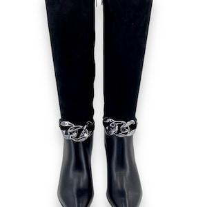 Könnte beinhalten: Schwarze kniehohe Stiefel mit spitzer Zehenpartie und silberner Kette am Knöchel. Der obere Teil ist aus weichem, schwarzem Wildleder, der untere Teil aus glattem, schwarzem Leder. Mit Reißverschluss.