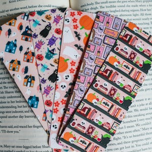 May include: Five rectangular bookmarks featuring Halloween-themed patterns on a light pink background. Designs include haunted houses, ghosts, pumpkins, bats, skulls, potion bottles, books, and stamps with the text Spooky printed on them.