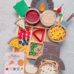 May include: Wooden pizza-making play set with various components, including pizza slices, toppings, dough, and a menu card. The set includes a pizza oven, a spatula, and containers of play dough. The menu card shows prices for pizza slices and whole pizzas.