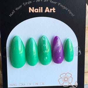 以下が含まれることがあります： 緑と紫の光沢のある、さまざまな形のつけ爪5本セット。「Nail Art」の文字がパッケージに表示されています。