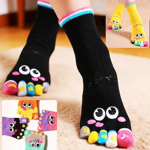 May include: Black toe socks with cartoon faces and colorful toes. The socks have a white, pink, and blue striped cuff. Additional socks in yellow, purple, orange, and green are also shown.