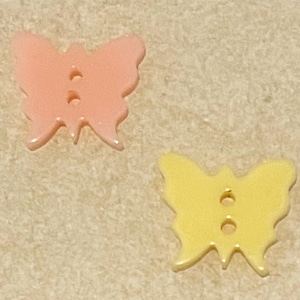 May include: Two plastic butterfly buttons, one pink and one yellow. The buttons have two holes each.