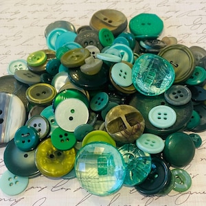 May include: A collection of various green buttons in different shades and sizes. The buttons are made of different materials, including plastic and glass, and have two or four holes. Some buttons are translucent, while others are opaque.