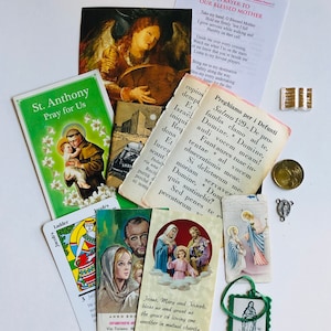 May include: A collection of religious imagery, including prayer cards, holy cards, and a small statue of the Virgin Mary. The cards feature images of saints, such as St. Anthony, and include prayers and religious text. The statue is made of metal and has a green and gold finish.