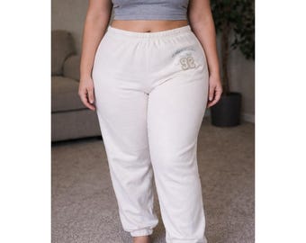 Pantalones deportivos Abercrombie & Fitch color crema con logo gráfico, estilo años 20, talla grande.