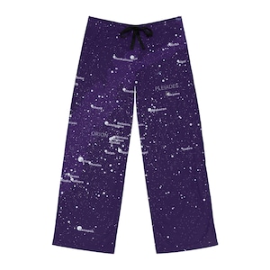 May include: Purple pajama pants with a celestial design featuring constellations like Orion and Pleiades. The pants have a drawstring waist and a pattern of white stars and constellation names. The fabric appears soft and comfortable.