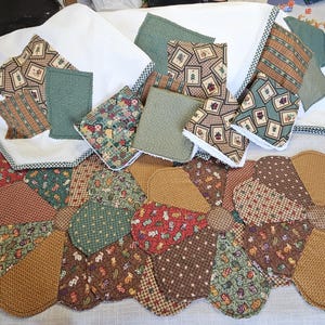 May include: A collection of handmade quilted items, including a floral-shaped table runner and matching coasters. The fabrics feature various patterns in shades of brown, green, and red, creating a rustic, country aesthetic.