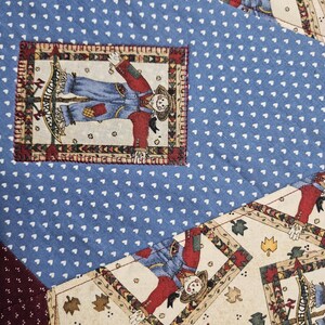 Op de afbeelding: Een patchwork quilt met blauwe stof met een wit hartjespatroon, cr&egrave;mekleurige stof met herfstbladmotieven en donkerbordeauxrode stof met witte stippen. Rechthoekige patches tonen vogelverschrikkers met de tekst "HARVEST".
