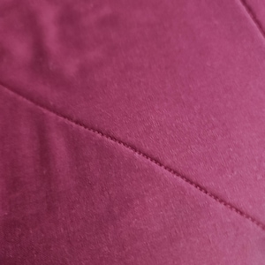 Op de afbeelding: Een effen diep magenta stof met een diagonale naad die over het oppervlak loopt. Het materiaal heeft een gladde, matte textuur met een consistente kleur en toont een strakke stiklijn waar twee delen van het textiel samenkomen.