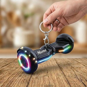 May include: Black hoverboard keychain with a silver keyring and clasp. The keychain has colorful LED lights on the wheels and sides. The word "Name" is printed on the top of the hoverboard.
