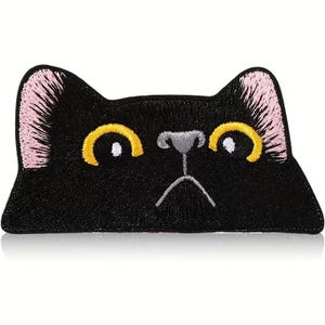 May include: Black cat face patch with embroidered details. Features yellow eyes, pink ears, and a gray nose. The patch is a rectangular shape, perfect for adding to clothing or accessories.