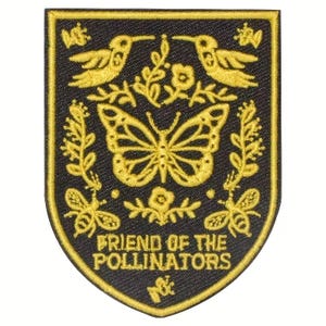 May include: Embroidered patch with a black background and a gold border. The design features a butterfly, two hummingbirds, bees, and floral elements. The text "FRIEND OF THE POLLINATORS" is at the bottom.