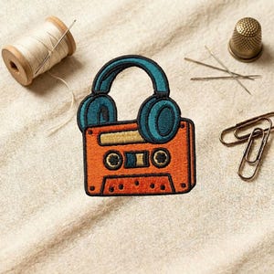 May include: An orange and teal embroidered patch featuring a cassette tape with headphones. A wooden spool of thread, needles, a thimble, and paper clips are also present, suggesting a sewing or crafting theme.