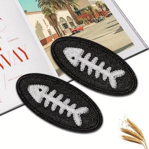 May include: Two black oval patches with a white embroidered fish skeleton design. The patches are placed on a magazine page with the word "California" visible. The patches are likely for clothing or accessories.