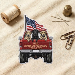 May include: An embroidered patch featuring a red pickup truck with three dogs in the bed, a waving American flag, and the text USA 250th Anniversary 1776-2026. The patch is surrounded by a spool of thread, a metal thimble, needles, and paper clips.