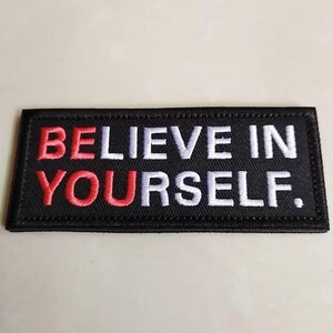 May include: Black rectangular patch with the embroidered text "BELIEVE IN YOURSELF." The words "BELIEVE IN" are white, and "YOURSELF" is red. The patch has a black border.