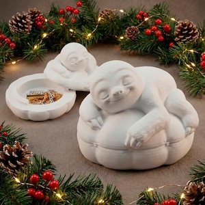 May include: White ceramic sloth jewelry box with a lid, and a smaller sloth figurine. The jewelry box is open, revealing gold-colored jewelry. The sloth is smiling and resting on a pumpkin-shaped base. Festive holiday decor surrounds the items.