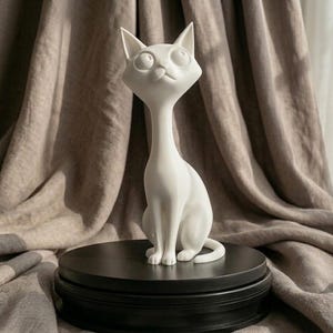 Puede incluir: Una figura de gato de cerámica blanca con cuello alargado y ojos grandes, sentada sobre un pedestal negro escalonado. El gato tiene un diseño caprichoso y de dibujos animados y está sobre un fondo de tela de tonos neutros.