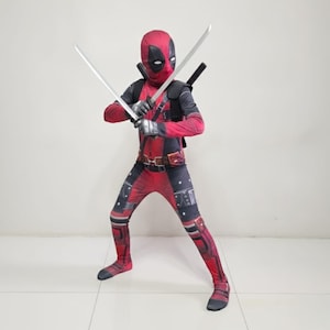 May include: A Deadpool costume featuring a red and black bodysuit, mask, and two silver toy swords. The costume includes a utility belt and shoulder straps. The character is in a fighting stance.