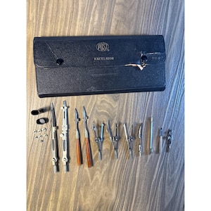 May include: A black leatherette case labeled POST EXCELSIOR containing a set of silver metal drafting instruments. The collection includes various compasses, dividers, ruling pens with brown handles, small metal screws, and caps for the tools.
