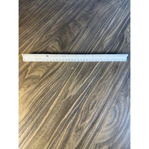 May include: A white triangular architectural scale ruler featuring black numerical markings and graduation lines along its three sides, designed for precise technical drafting and measurement tasks in imperial units of inches.