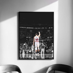 Puede incluir: Impresión enmarcada en blanco y negro de un jugador de baloncesto con el número 30, levantando el brazo en señal de celebración. La imagen captura un momento del juego, con el público de fondo.