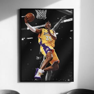 Puede incluir: Fotografía en blanco y negro enmarcada de un jugador de baloncesto en acción, vistiendo una camiseta amarilla y morada con el número 24. El jugador está en el aire, a punto de lanzar el balón hacia el aro. La imagen es un retrato.