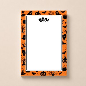 May include: A rectangular notepad featuring a white centre panel with the word BOO! printed at the top. The border is orange and decorated with a repeating black pattern of ghosts, pumpkins, bats, cats, witches' hats, and bare trees.