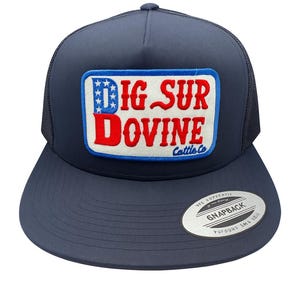 May include: Navy blue trucker hat with a curved brim and mesh back. The front patch reads "BIG SUR DOVINE Cattle Co" in red and white lettering with blue stars. A "Snapback" sticker is on the brim.