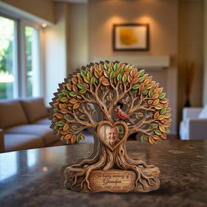 Könnte beinhalten: Ein hölzernes Gedenkbaum mit einem herzförmigen Fotorahmen. Der Baum hat detaillierte Äste und Blätter in Herbstfarben. Ein roter Kardinal sitzt auf einem Ast. Auf der Basis steht "In loving memory of Grandpa 1968-2026."