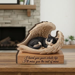 May include: A wooden memorial sculpture featuring a black and white cat sleeping inside a pair of carved angel wings. The name Oliver is engraved on the wing, and the base features the text: I loved you your whole life I'll miss you the rest of mine.