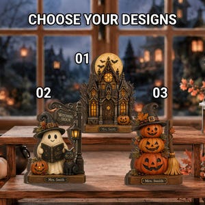Può includere: Tre decorazioni da tavolo a tema Halloween etichettate 01, 02 e 03 con il testo CHOOSE YOUR DESIGNS. Il design 01 è una casa stregata, lo 02 un fantasma con un gatto e un cartello WITCHING HOUR, lo 03 tre zucche impilate con un cappello.