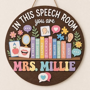 May include: A round dark wood wall sign featuring the text IN THIS SPEECH ROOM you are and MRS. MILLIE. The design includes colourful illustrations of books labelled HEARD, BRAVE, CAPABLE, GROWING, VALUED, SMART, CONFIDENT, KIND, plus flowers, speech bubbles, and icons.